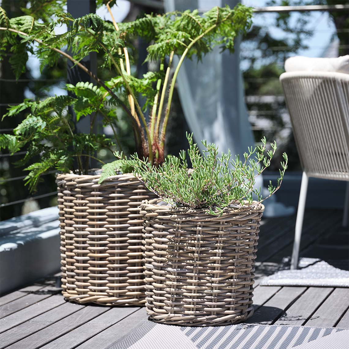 La fioriera da giardino SEGLA in rattan intrecciato è disponibile in due misure Cesti per piante da giardino in rattan naturale con piante sul patio soleggiato